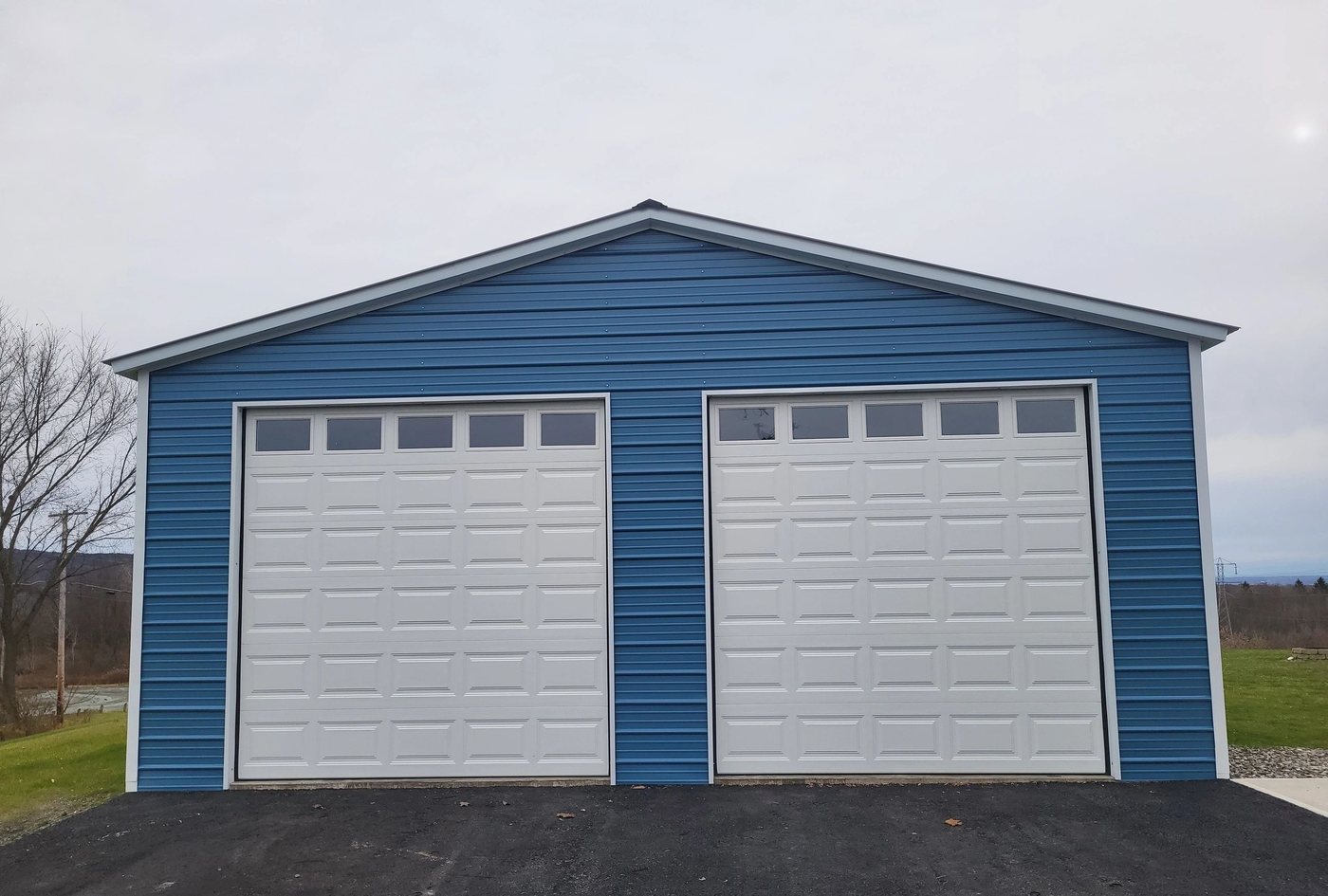 Two white doors set into a blue steel pole barn, open field either side.