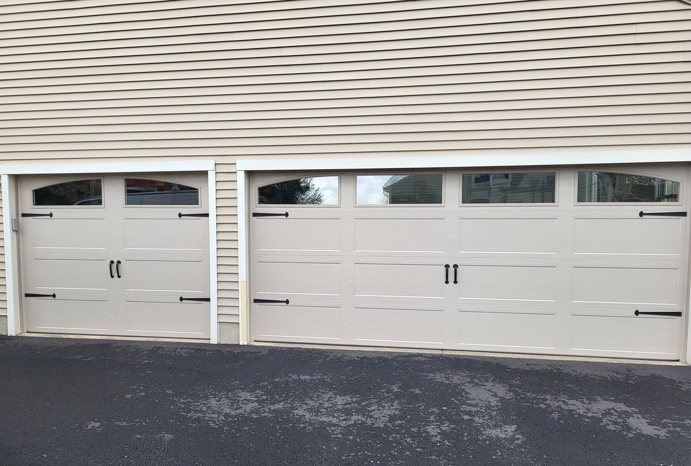 Two carriage-style doors in cream, arched window rows and strap hardware, on fresh asphalt.