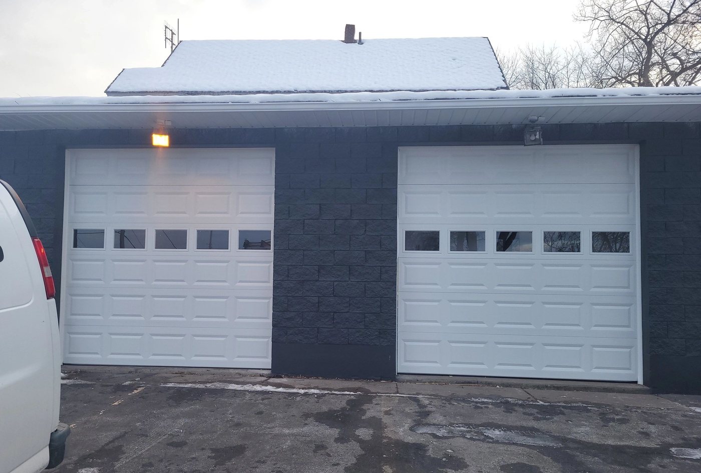 Two white doors of different heights in a charcoal building front.