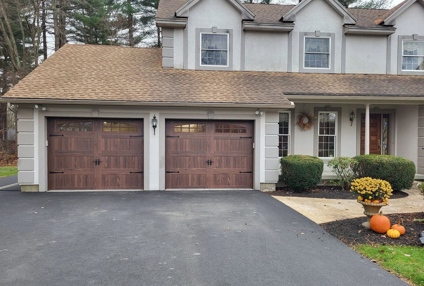 Two woodgrain doors on a two-story house, pumpkins and mums out front.