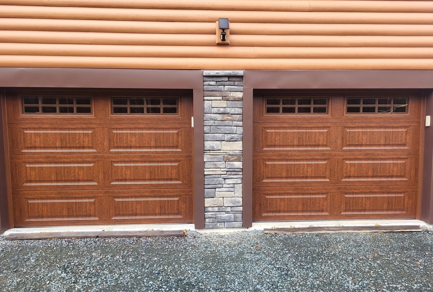 Two woodgrain doors with long raised panels and square window rows, either side of a stone column.