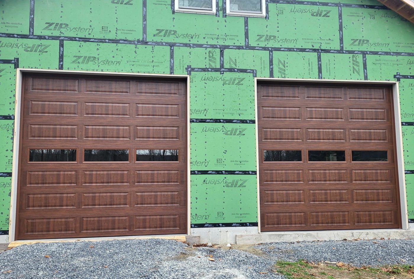 Two woodgrain doors hung in a building still in green sheathing, before the siding goes on.