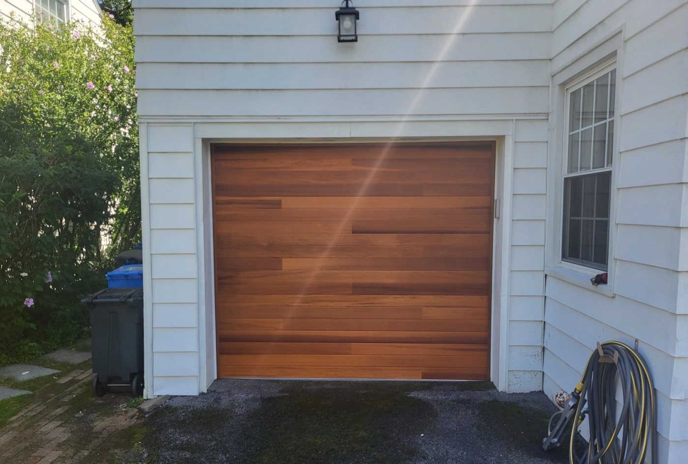 A single natural wood-look door in white siding, coach lamp above it.